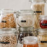 Glass jars filled with diverse kitchen ingredients like rice and chickpeas on a white background.